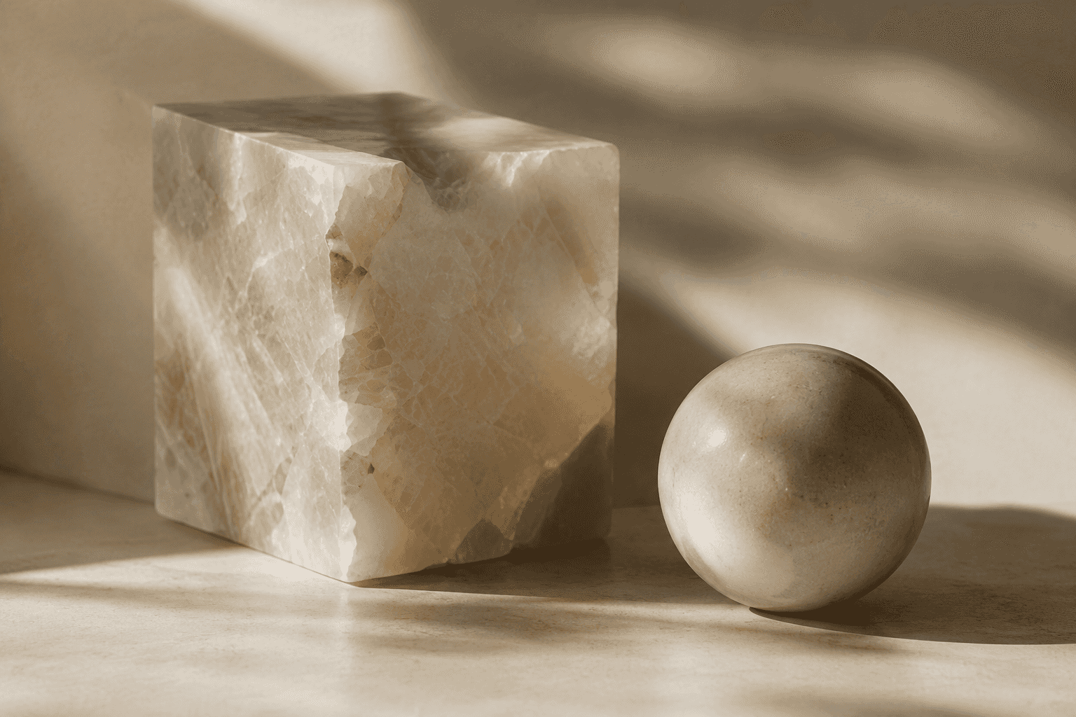 A carved marble cube and a marble sphere standing side by side in raking light.