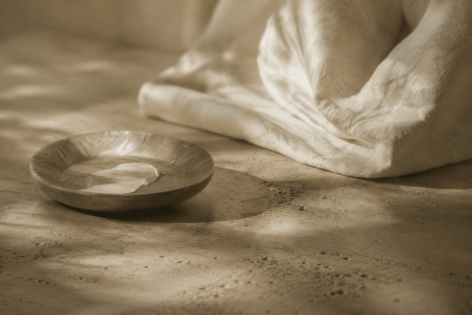 A small marble dish beside folded pale linen, photographed in soft warm light.