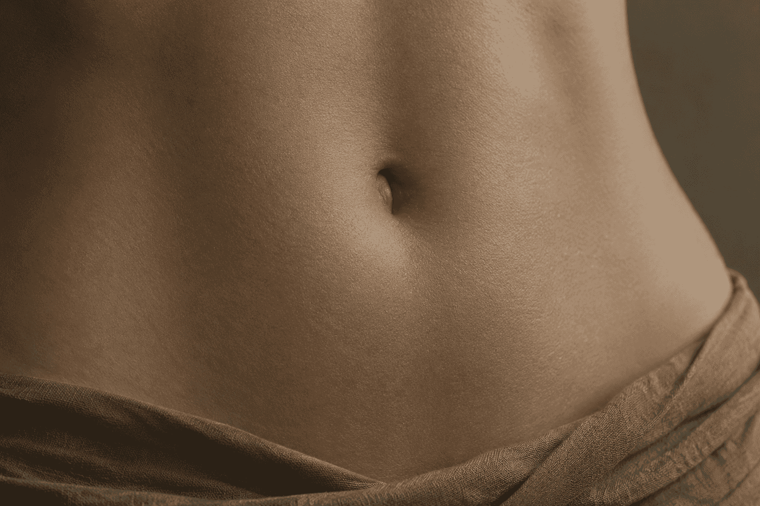 A close view of an abdomen and navel, with pale fabric draped loosely at the waist.