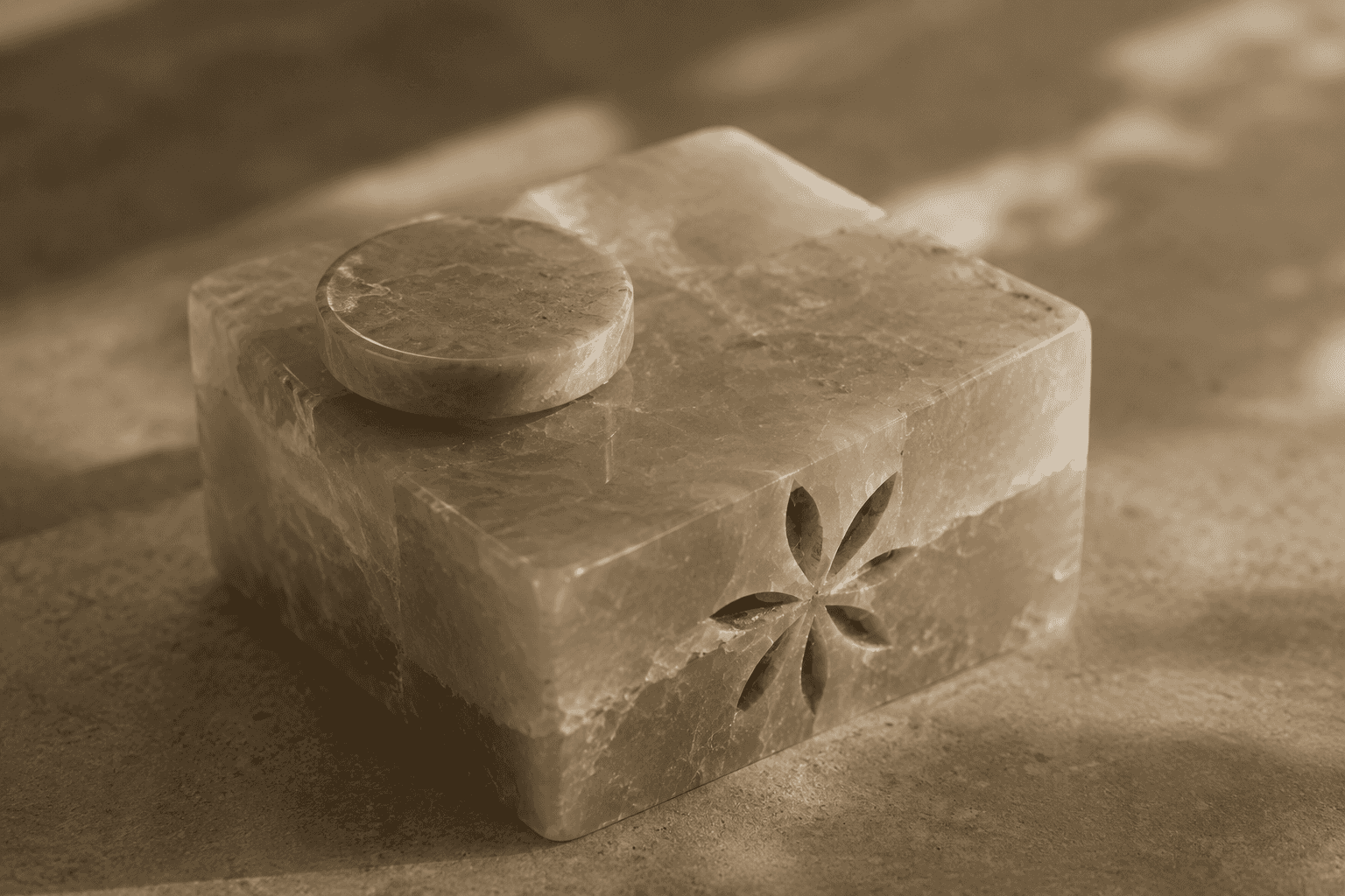 A small carved marble box with a round lid and an etched flower motif on one face, photographed in soft light.